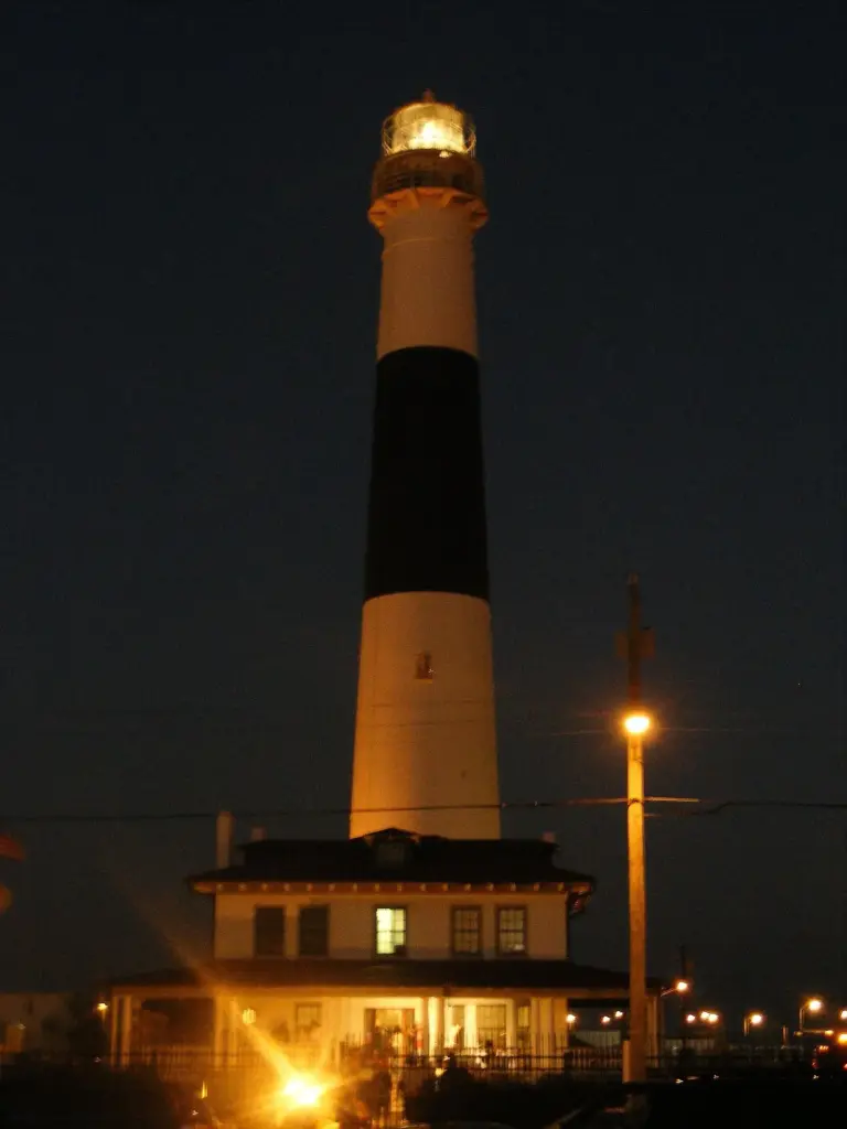 The tall banded Absecon Lighthouse tower lit up at dusk above the lightkeeper's house