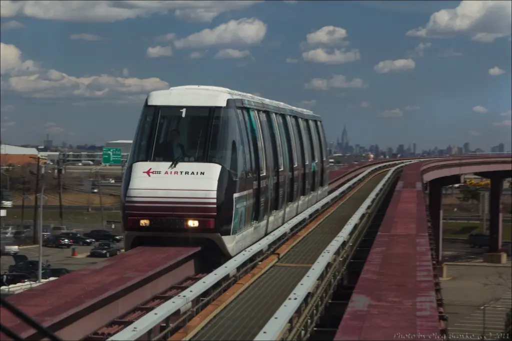 A white and maroon AirTrain car on its elevated guideway, with the Manhattan skyline and the Empire State Building on the horizon
