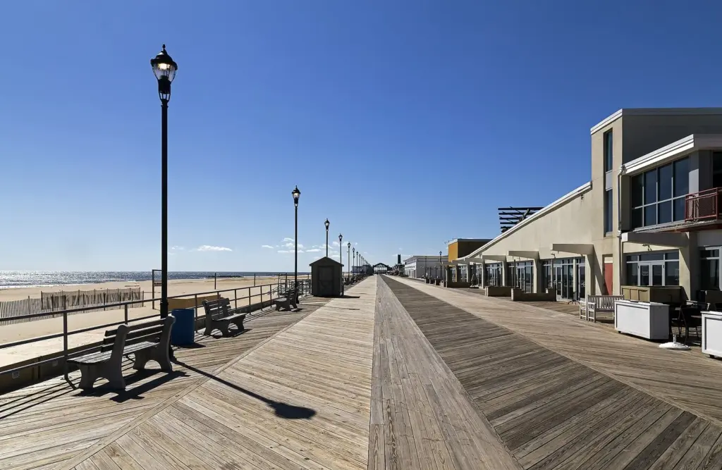 The wide wooden boardwalk at Asbury Park under a blue sky, with the beach and ocean on the left and the old Casino in the distance
