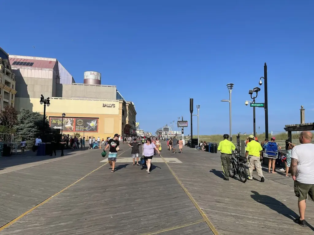 The wide wooden Boardwalk stretching north past Bally's, with walkers, benches, lampposts and the dunes to the right