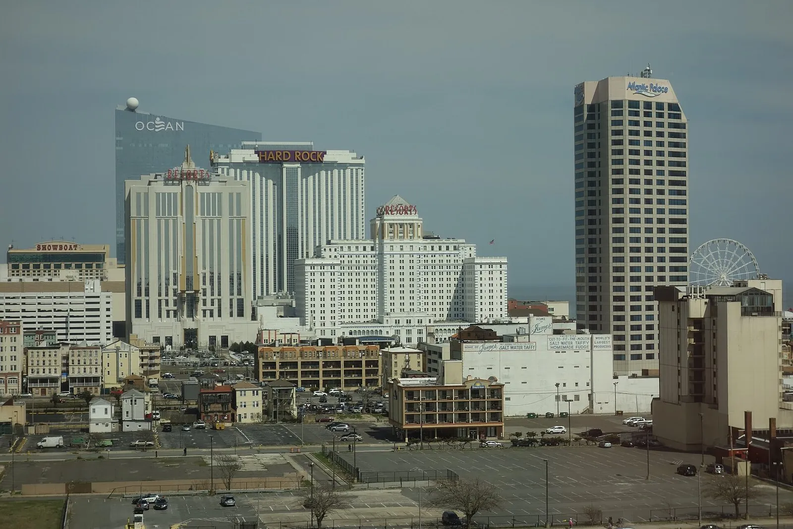 Atlantic City casinos at the north end of the Boardwalk: Ocean's glass tower, the Hard Rock and the two Resorts towers rising behind parking lots, with a Ferris wheel at right