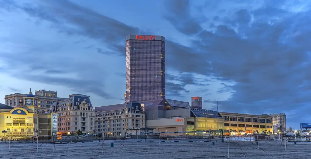 Bally's tall hotel tower rising behind a row of lit Boardwalk buildings at dusk, seen from the beach