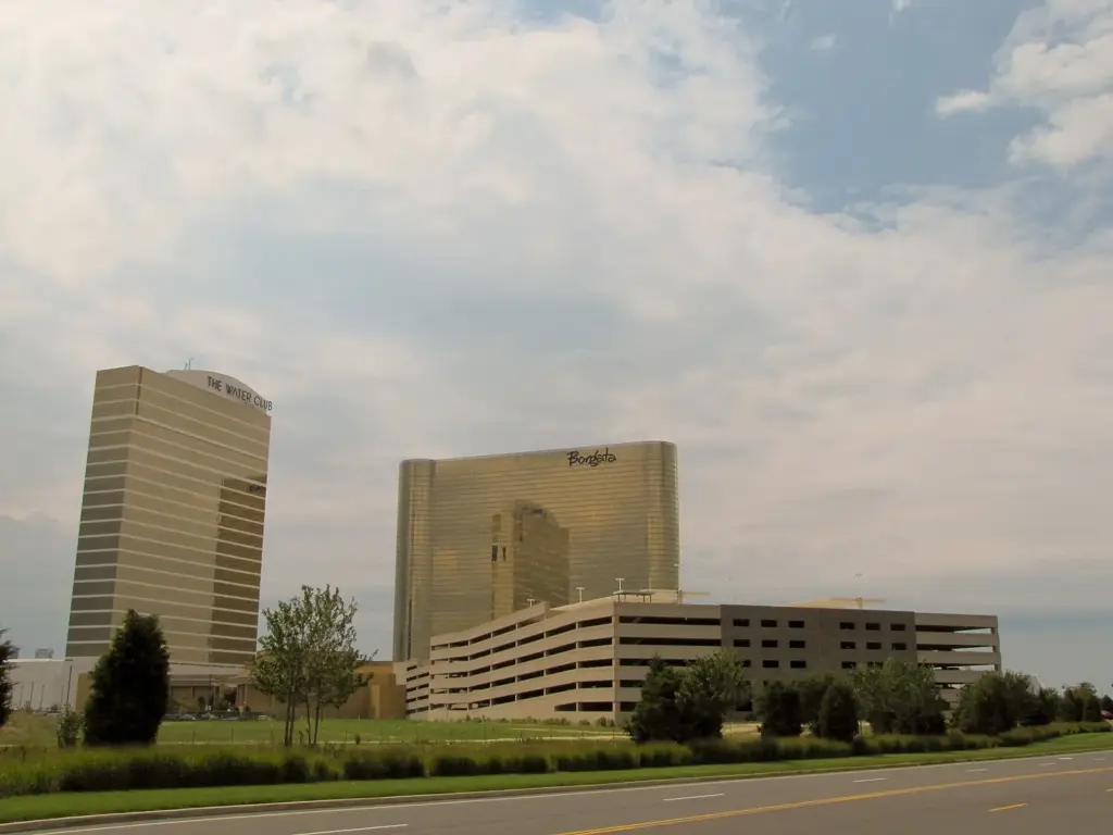 Borgata's gold glass hotel tower beside the tan tower now called MGM Tower, with a parking garage, trees and a road in front