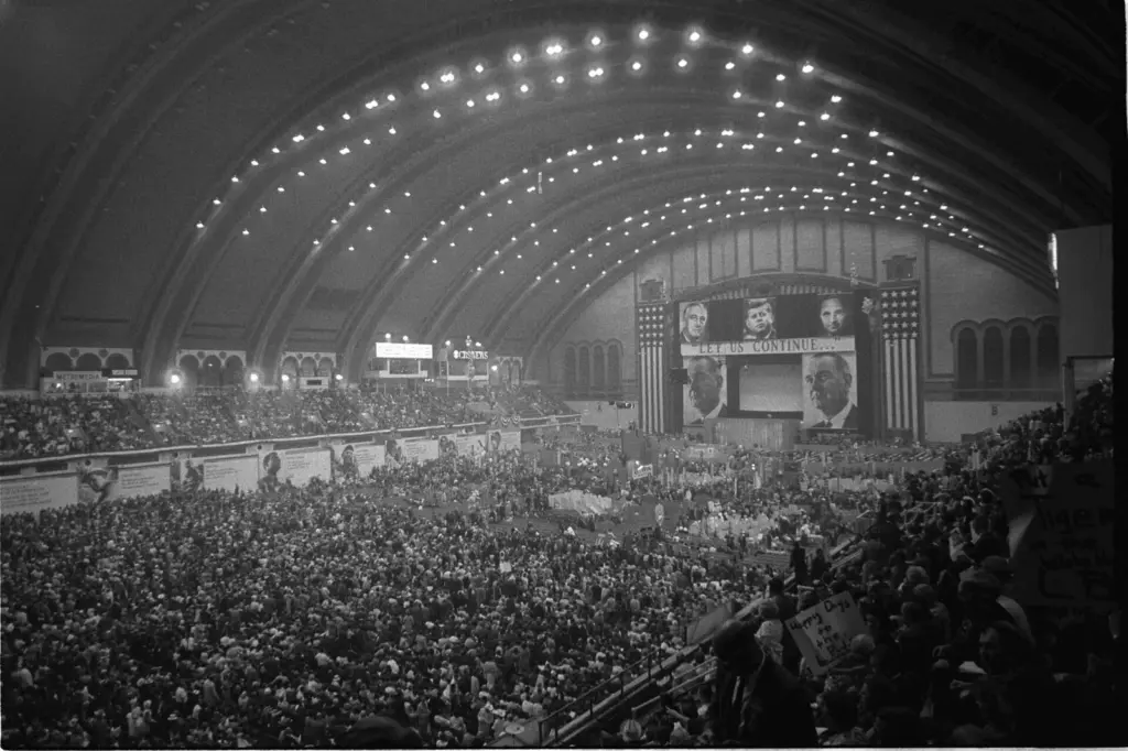 A packed arena under a vast barrel-vaulted ceiling, with delegates on the floor and crowds in the balconies