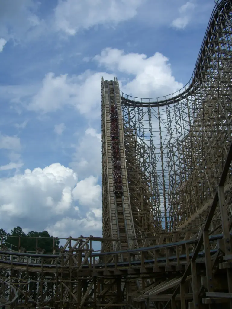A coaster train cresting the tall wooden lift hill of El Toro against a blue sky with white clouds