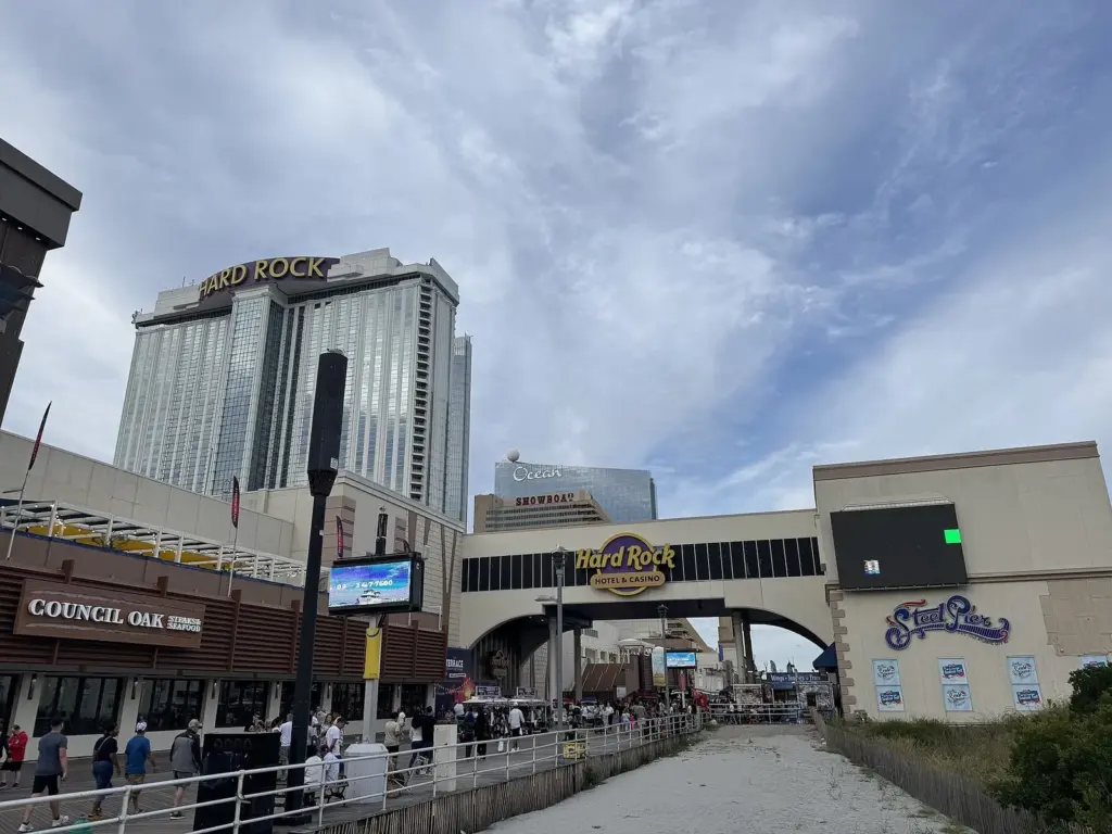 Hard Rock's tower and its Boardwalk entrance arch, with people walking on the Boardwalk under a cloudy blue sky