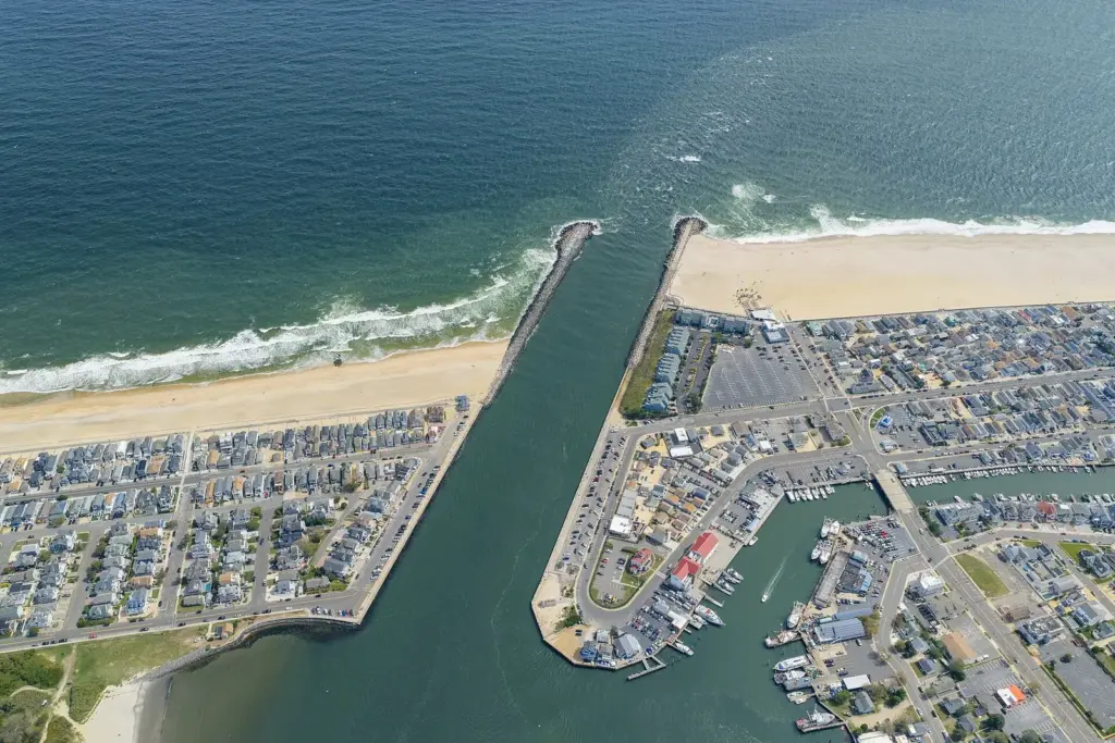 Aerial view of the Manasquan Inlet, a straight channel between two rock jetties, with Manasquan's beach and houses on one side and Point Pleasant Beach's marinas on the other