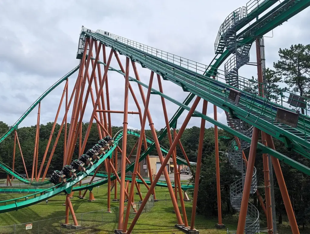 A floorless coaster train rounding a curve beneath green track and orange steel supports