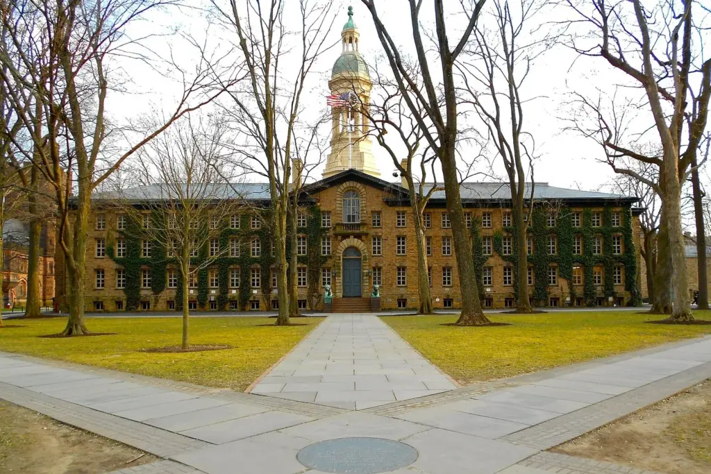 Nassau Hall at Princeton University, a long stone building with a cupola, at the end of a stone walk lined with bare trees