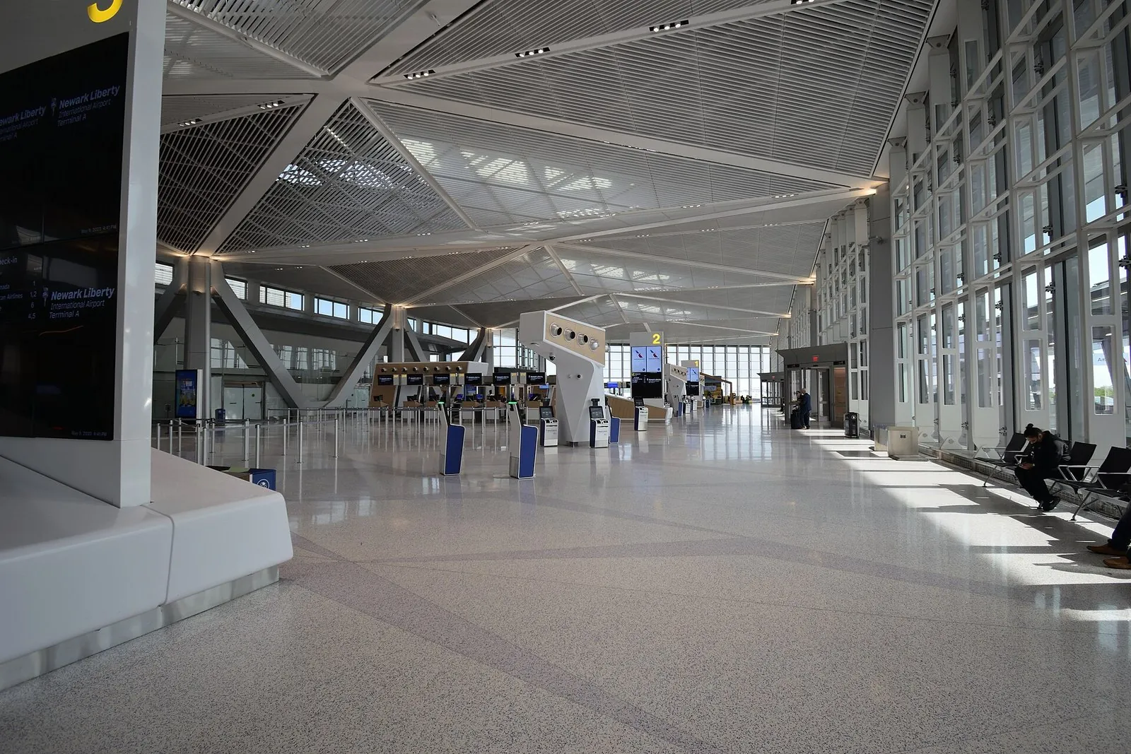 Newark Airport's new Terminal A, a bright, high-ceilinged departures hall with angled white roof beams, check-in kiosks and tall windows