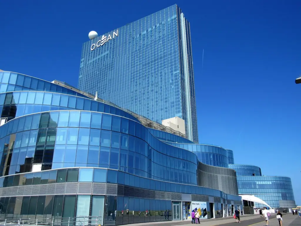 Ocean's tall blue glass tower with the word OCEAN near the top, above a curving blue glass podium and people on the Boardwalk