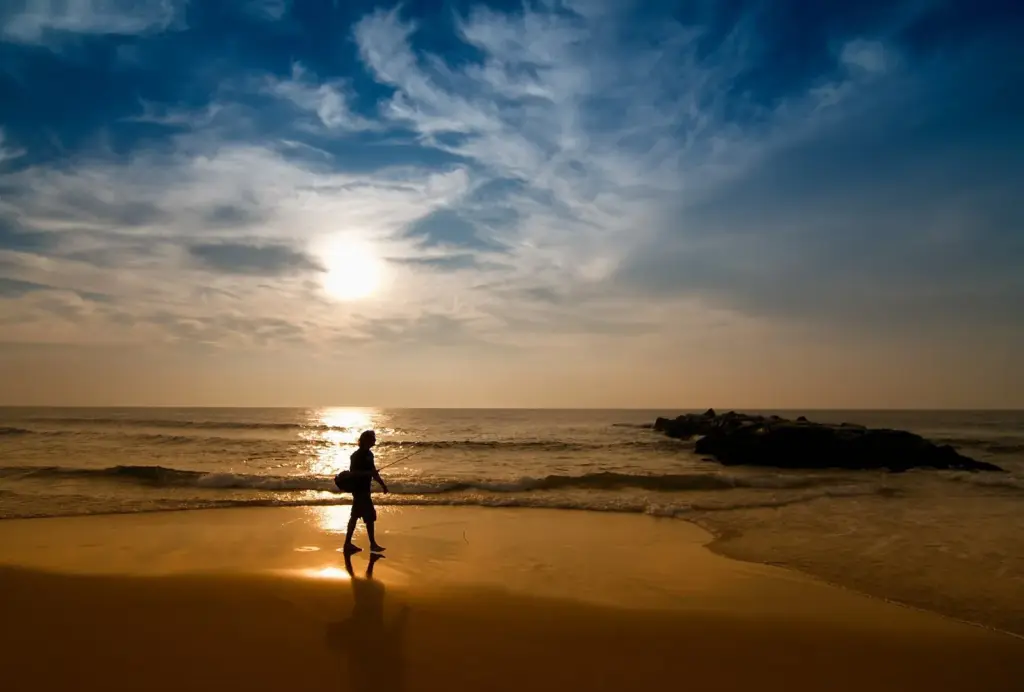 A lone walker silhouetted on the wet sand at sunrise on the beach at Spring Lake, with a rock jetty in the water