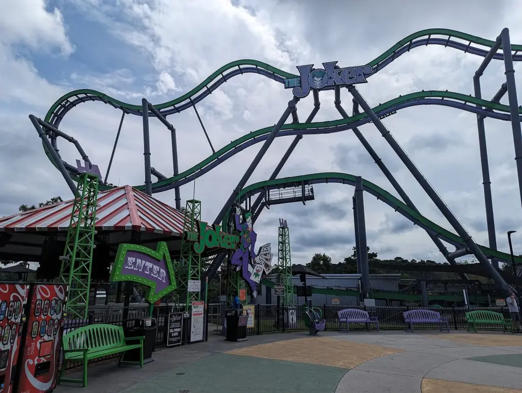 The purple and green track of The Joker coaster looping over its entrance plaza and benches