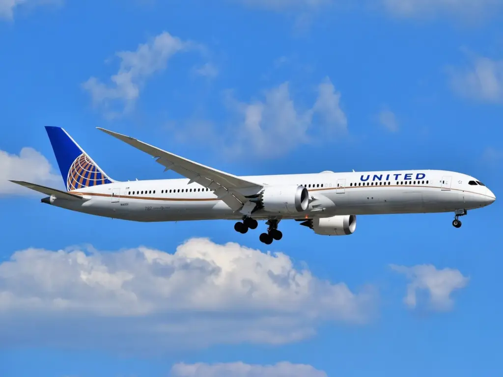 A United Airlines Boeing 787 Dreamliner with its landing gear down against a blue sky with scattered clouds