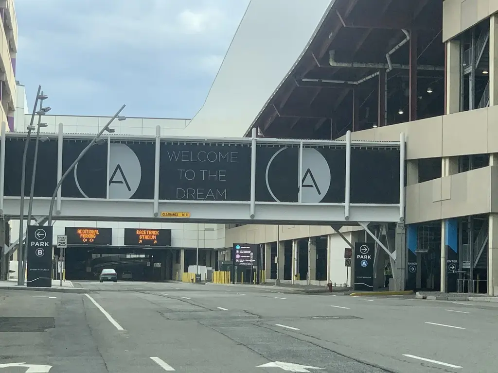 A pedestrian bridge reading Welcome to the Dream spanning the entrance to a multi-level parking deck, with Park signs and an empty road in front