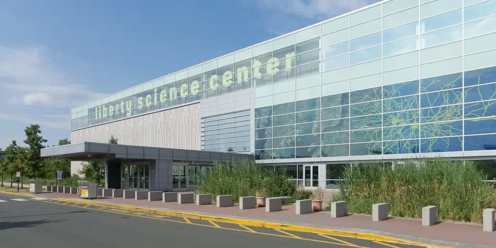 The long glass front of the Liberty Science Center building with its name in green lettering, beside a drop-off lane and landscaped beds