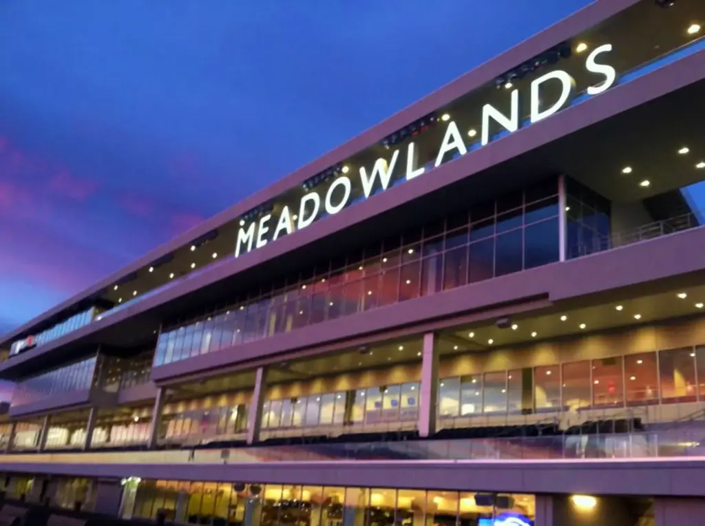 The racetrack's glass-fronted grandstand at dusk, with the word Meadowlands lit across the top under a purple sky