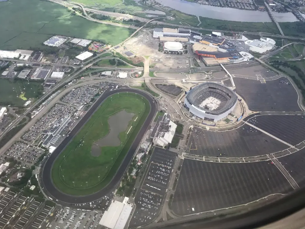 Aerial view of the Meadowlands complex: the round stadium surrounded by parking lots, an oval racetrack to its left and the colorful American Dream mall buildings beyond