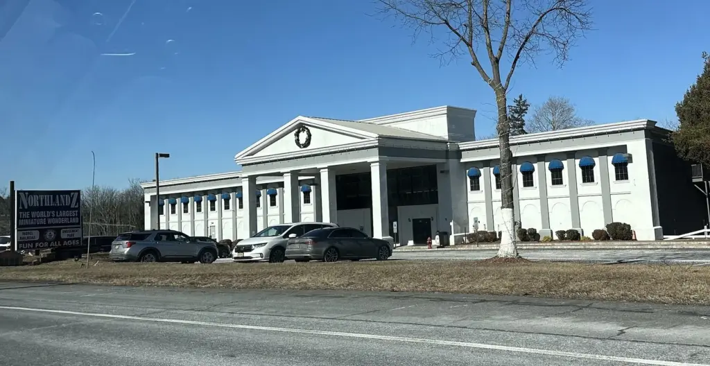 The white columned front of the Northlandz model railroad building beside Route 202, with a few cars parked in front on a sunny winter day