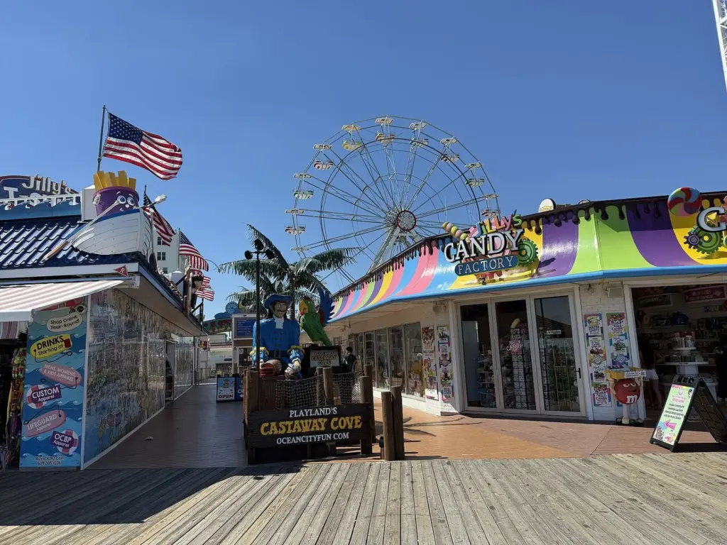 The boardwalk entrance to Playland's Castaway Cove, with a pirate and parrot statue above the park sign and a Ferris wheel rising behind it, between a candy shop and a T-shirt shop