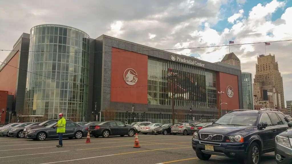 The glass and red-paneled front of Prudential Center in downtown Newark, with a parking attendant in a yellow vest and an Art Deco office tower behind