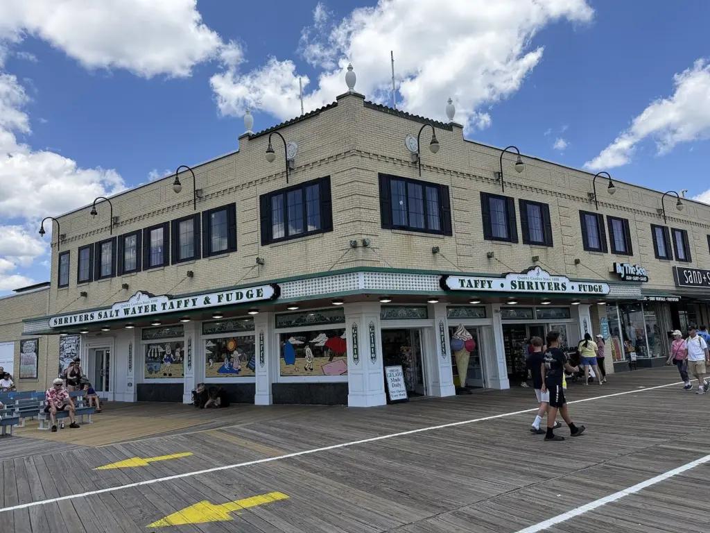 Shriver's Salt Water Taffy and Fudge, a two-story tan brick corner building on the boardwalk with green-and-white signs over its windows and cartoon beach scenes painted on the glass