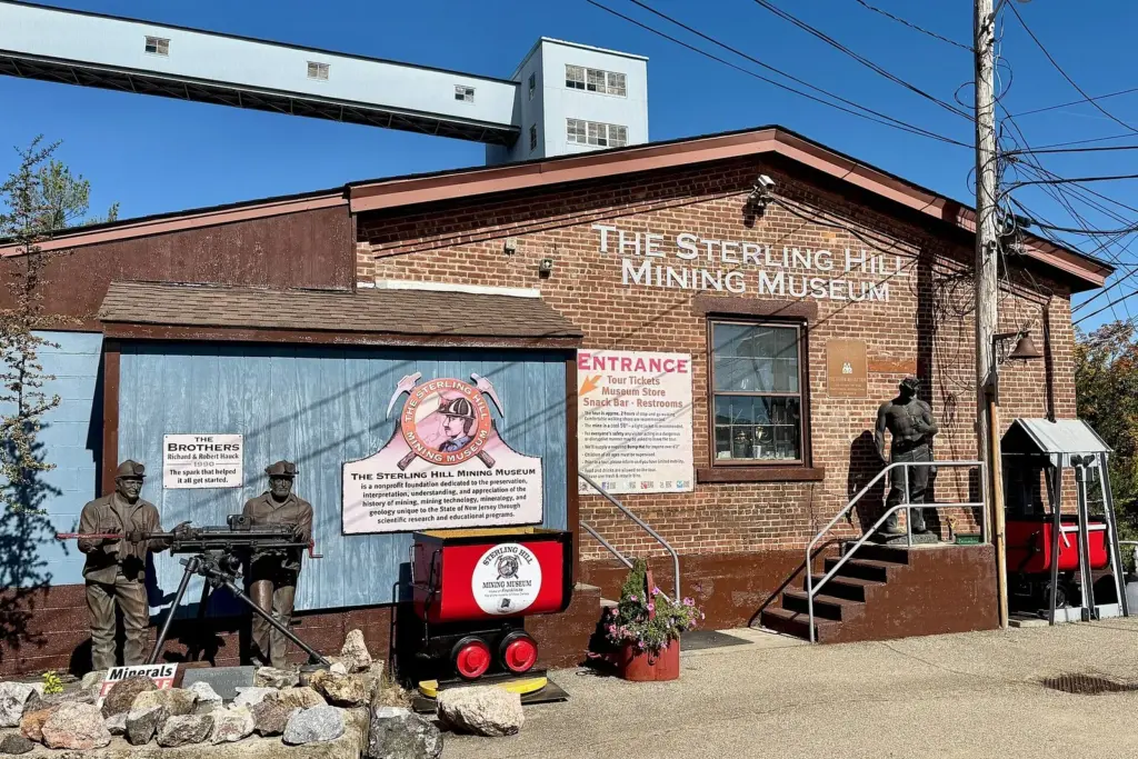 The brick Sterling Hill Mining Museum building with its painted sign, statues of miners and a red ore cart out front, under a blue sky